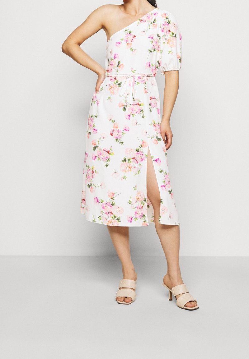 White floral dress featuring one-shoulder design, elastic waist, and side slit. Floral pattern in pink and green. Paired with nude heeled mules.