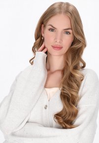 Jasnoszary, fakturowany kardigan o luźnym kroju, z zapięciem na guziki i prążkowanymi mankietami. Model ma długie, falowane włosy ułożone przy twarzy.