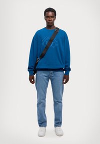 Blue sweatshirt with a graphic print, paired with light blue jeans and white sneakers. Includes a black shoulder strap bag.