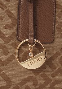 Borsa marrone con texture, caratterizzata da un dettaglio di ferramenta circolare dorata con incisione "LIU-JO" e un piccolo dettaglio di pietra preziosa.