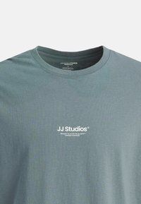 Gråblå crew neck T-shirt med hvid "JJ Studios" logo og lille tekst centreret på brystet, lavet af økologisk bomuld, størrelse large.