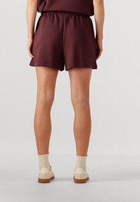 Pantalones cortos burdeos con cinturilla elástica, combinados con zapatos beige y calcetines color crema con un borde rizado. Textura de tejido suave.