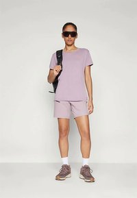 Αθλητικό μπλουζάκι και σορτσάκι σε ανοιχτό μωβ χρώμα, και τα δύο κατασκευασμένα από αναπνεύσιμο ύφασμα. Συνδυασμένα με καφέ αθλητικά παπούτσια και μαύρα γυαλιά ηλίου.