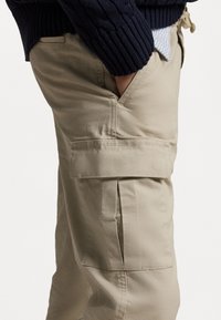 Beige cargo pants with a relaxed fit, featuring side pockets and a tapered leg. Smooth cotton fabric with minimal stitching details.