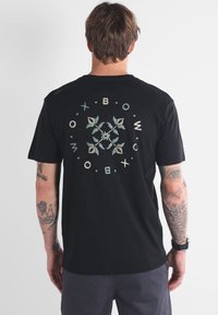 T-shirt noir à manches courtes avec un design botanical circulaire en vert doux et beige au dos, fabriqué dans un tissu doux et respirant.