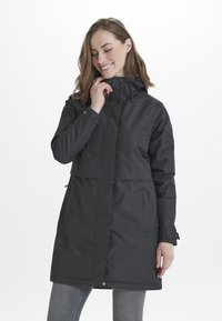 Giacca impermeabile nera con cappuccio, dotata di bottoni frontali, tasche laterali con zip e polsini regolabili. Tessuto liscio, design di lunghezza media.