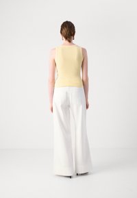 Yellow ribbed tank top paired with white wide-leg pants. The outfit features a fitted design and smooth texture, emphasizing a minimalist style.