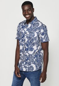 Camicia a maniche corte, con bottoni, in bianco e blu con motivo floreale. Presenta una tasca sul petto e una vestibilità rilassata. Realizzata in tessuto leggero.
