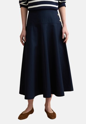 Donna che indossa una gonna midi a linea a trapezio blu navy con bottoni laterali, abbinata a un maglione a righe e ballerine in suede marrone.