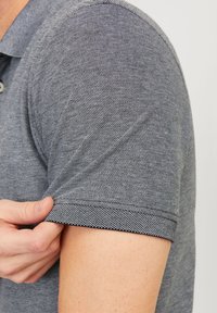 Gray knitted polo shirt with a textured pattern, short sleeves, and a classic collar; visible stitching detail along the sleeve edge.