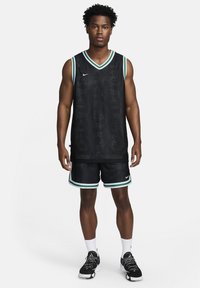 Camiseta de baloncesto negra con acentos verdes, con un escote en V y textura de malla. Combinada con pantalones cortos a juego y zapatillas deportivas negras.