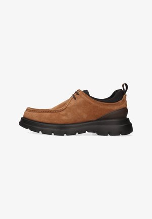 Brune ruskind slip-on sko med rund tå, syet detaljering og en sort gummisål med fremtrædende slidbanemønstre.