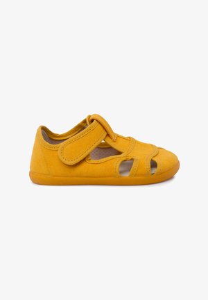 Pantofii Mary Jane din material galben au o curea ajustabilă Velcro, decupaje deschise pe laturi și o talpă flexibilă.
