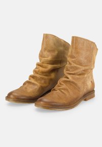 Par de botas de ante color marrón claro hasta la mitad de la pantorrilla, con diseño suelto, punteras redondeadas y suelas planas marrones, mostradas sobre un fondo blanco.