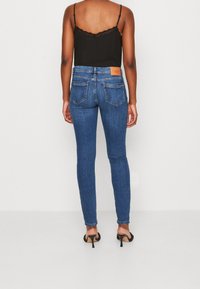 Úzké džíny v tmavě modrém denimu s mírným zvýšením pasu, se zadními kapsami a koženým štítkem značky na pásku.