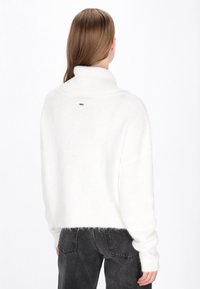 Witte, fluffy coltrui met een cropped zoom en geribbelde manchetten, voorzien van een klein zwart accent bij de achterkant van de halslijn. Gekocht met donkere jeans.