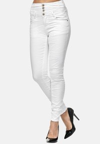 Jeans blancos, ajustados y de cintura alta, con cuatro botones metálicos y una textura lisa, ligeramente arrugada. Combinados con tacones altos negros.