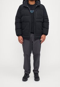 Czarna kurtka puchowa z kapturem, zapinana na zamek, z bocznymi kieszeniami, noszona na czarnym t-shircie i ciemnoszarych spodniach, w połączeniu z czarnym obuwiem.