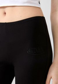 Zwarte leggings van rekbare stof, met een geborduurd "Von Dutch" logo in een bijpassende kleur nabij de tailleband. Soepele textuur en pasvorm.