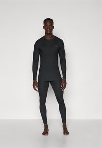 Juodas ilgomis rankovėmis termo marškinėliai ir prigludę leggingai iš elastinio audinio, su subtiliu logotipu ant krūtinės ir sklandžiu paviršiumi.