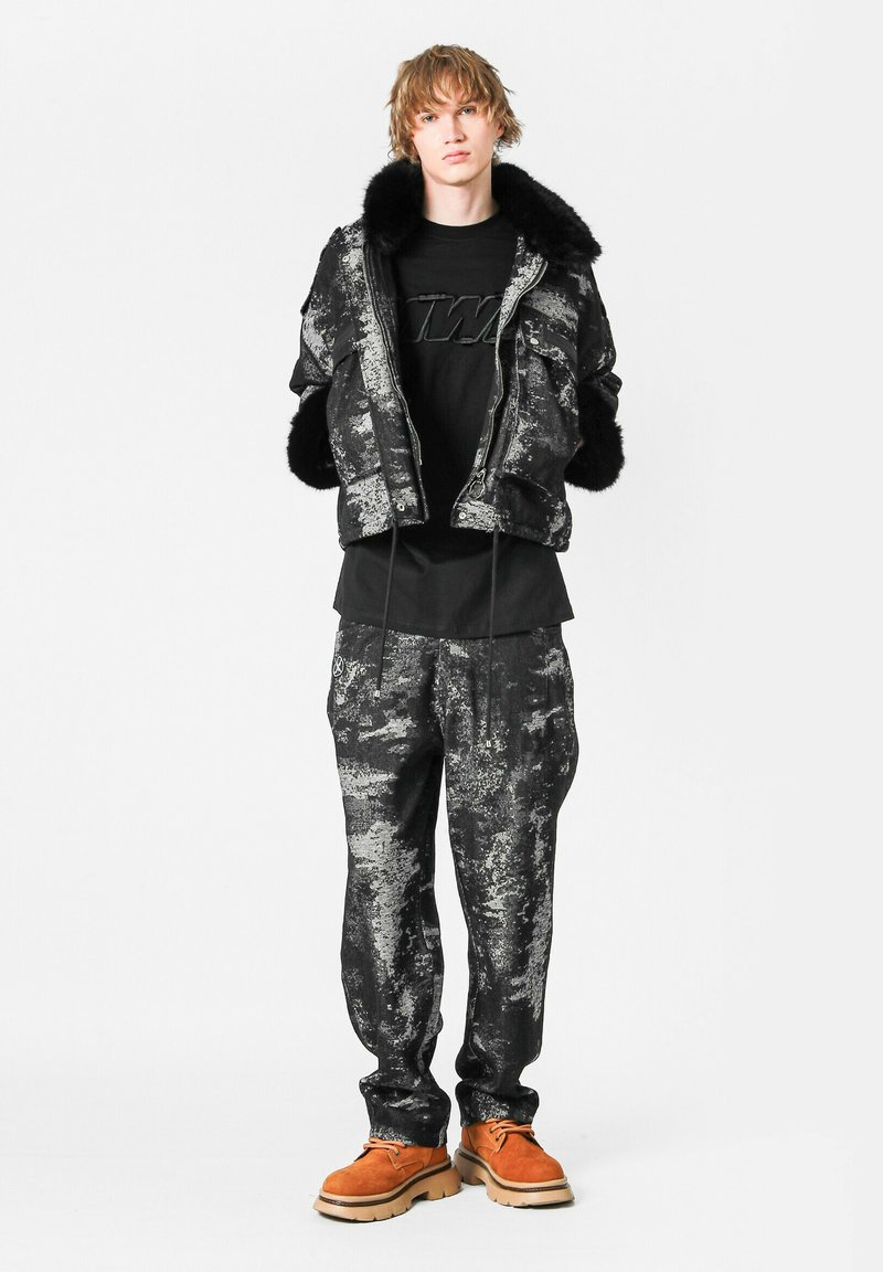 Chaqueta de patrón negro y gris con acentos de piel, combinada con una camiseta negra y joggers a juego. Zapatos marrones con suelas gruesas.