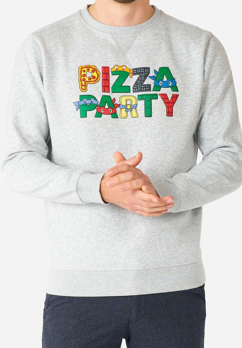 Sweat-shirt gris avec le texte coloré "PIZZA PARTY" comprenant des pizzas et des visages de tortues dessinés sur les lettres, porté par une personne aux mains jointes.