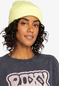 Gorro de canalé amarillo neón, diseño ajustado, textura suave, combinado con una camiseta gráfica oscura que presenta letras coloridas y acentos florales.