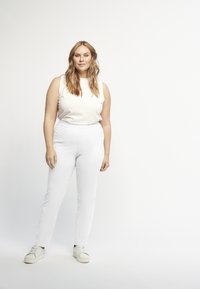 Witte geribbelde mouwloze top gecombineerd met strakke witte broek. Model draagt witte sneakers. Eenvoudig ontwerp met een gladde, cleane textuur.