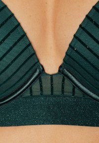 Bra verde scuro con una profonda scollatura a V, variazioni di texture, delicate righe e un elastico glitterato nella parte inferiore per un tocco di dettaglio in più.