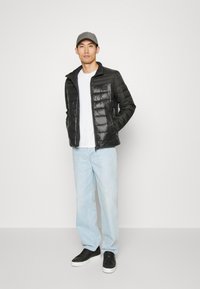 Giacca a vento nera con zip frontale e texture trapuntata, abbinata a una maglietta bianca semplice e jeans azzurri chiari. Sneakers nere completano il look.