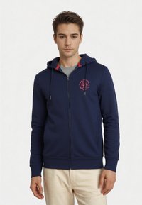Felpa con zip blu navy, logo frontale, dettagli a contrasto rossi sul cappuccio, maniche lunghe e due tasche laterali. Tessuto dalla texture liscia.