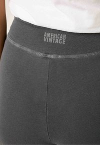 Sive legice s prilegajočo zasnovo in elastiko v pasu, ki vsebuje subtilen tisk z besedilom "AMERICAN VINTAGE". Gladka tekstura.