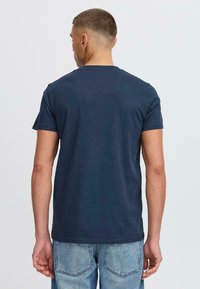 Tricou din bumbac de culoare bleumarin, cu mâneci scurte, gât rotund și o textură fină. Vederea din spate evidențiază un detaliu subtil al cusăturii.
