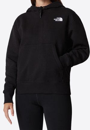 Woman wearing a black The North Face hoodie with front pocket, long sleeves, and drawstring hood, paired with black leggings.