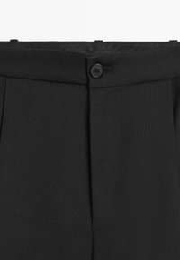 Schwarze Hose mit flacher Vorderseite, Einzelknopfverschluss und dezenten Falten; gefertigt aus glattem Stoff mit strukturierter Oberfläche.