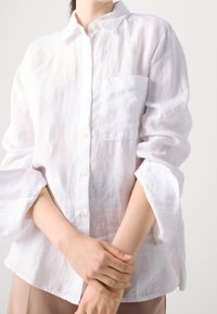 Witte, langmouwige linnen shirt met een knoopsluiting op de kraag, voorzien van een enkele borstzak en opgerolde mouwen. Zacht, gestructureerd materiaal.