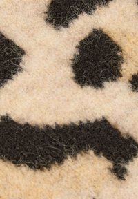 Tessuto di lana beige e nero con una texture pelosa, caratterizzato da un motivo astratto a macchie con forme irregolari e bordi morbidi e arrotondati.