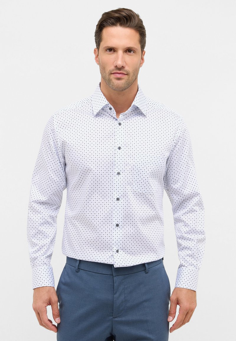 Camicia bianca a maniche lunghe con un motivo geometrico blu, colletto standard, chiusura frontale a bottoni e bottoni scuri a contrasto.