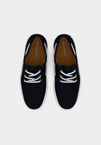 Ζευγάρι μαύρα παπούτσια τύπου boat από τον Karl Lagerfeld με λευκά κορδόνια και λευκές σόλες, φωτογραφημένα από πάνω σε απλό φόντο.