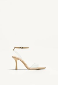 Klarheine Sandalen mit einem nude-farbenen Fußbett, ausgestattet mit einem transparenten Riemen und einem schmalen Knöchelriemen mit einer metallischen Schnalle. Glatte Oberfläche, spitze Zehen.