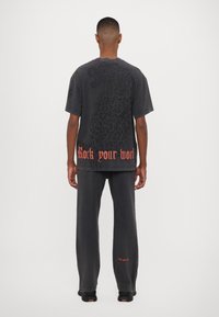 Tmavě šedé oversized tričko s velkým černým leopardím potiskem na zádech, se slovním spojením "Rock your world" v červeném písmu. V kombinaci s odpovídajícími kalhotami.