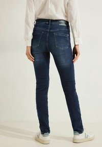Mörkblå denim skinny jeans med midja i normal höjd, femficksdesign och subtila ljusa blekningar. Matchat med vita sneakers.