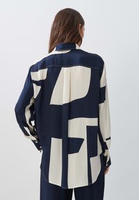 Navy and cream blouse in smooth fabric with geometric patterns, long sleeves, button cuffs, and a classic collar, viewed from the back.
