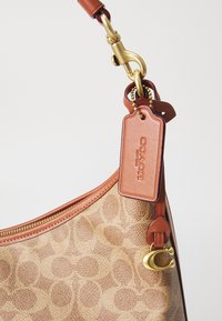 Borsa a mano in pelle marrone con un motivo, hardware dorato e un'etichetta abbinata. Presenta una forma curvilinea, chiusura con zip e accenti in pelle a contrasto.