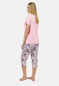 Jasnoróżowa bluzka z krótkim rękawem zestawiona z spodniami o długości trzech czwarte w kwiatowy wzór w delikatnych pastelowych kolorach. Wygodne dopasowanie i lekką tkanina.