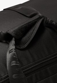 Un sac en tissu noir avec une fermeture éclair et un rabat en Velcro. Le matériau a une finition texturée, avec une sensation de durabilité et une sangle tissée.