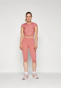 Rózsaszín sportos crop top és capri leggings elasztikus, sima tapintású anyagból, világos rózsaszín sportcipőkkel párosítva.