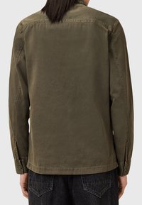 Olivgrüne, gebürstete Baumwolljacke mit geradem Schnitt, Knopfmanschetten und minimalen Nahtdetails, von hinten gezeigt.