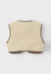 Ärmlös väst i krämfärgad fleece, med mjuk textur och bruna detaljer längs kanterna och ärmhålen.