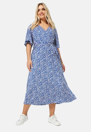 Blauwe wikkeljurk met een wit abstract patroon, korte wijde mouwen, een taille met elastiek en een vloeiende rok. Gecombineerd met witte sneakers.